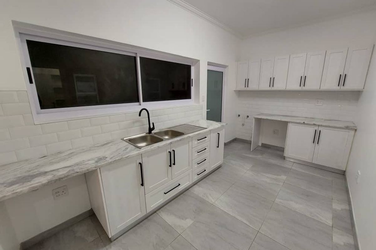 A modern, clean kitchen featuring white shaker-style cabinetry, marble-look countertops, subway tile backsplash, and a double basin sink with a contemporary black faucet.