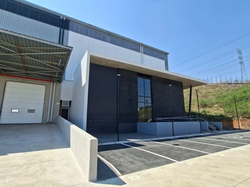 Modern industrial facility featuring a large roller shutter door, concrete loading area, dedicated parking bays, and contemporary architectural facade with full-height glazing.