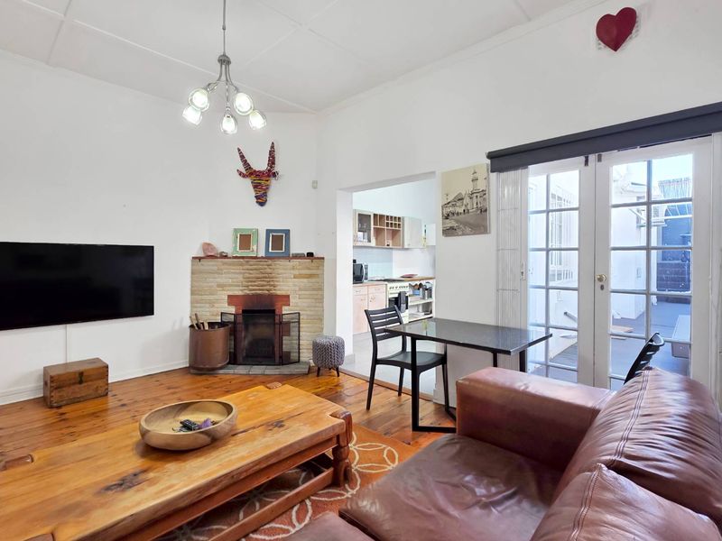 Open plan living area featuring hardwood floors, a brick fireplace, and direct access to an outdoor patio through classic french doors.