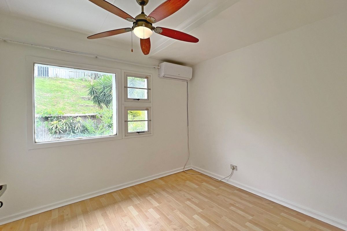 A bright, empty bedroom featuring light laminate flooring, a ceiling fan, and a wall-mounted split-system air conditioner.