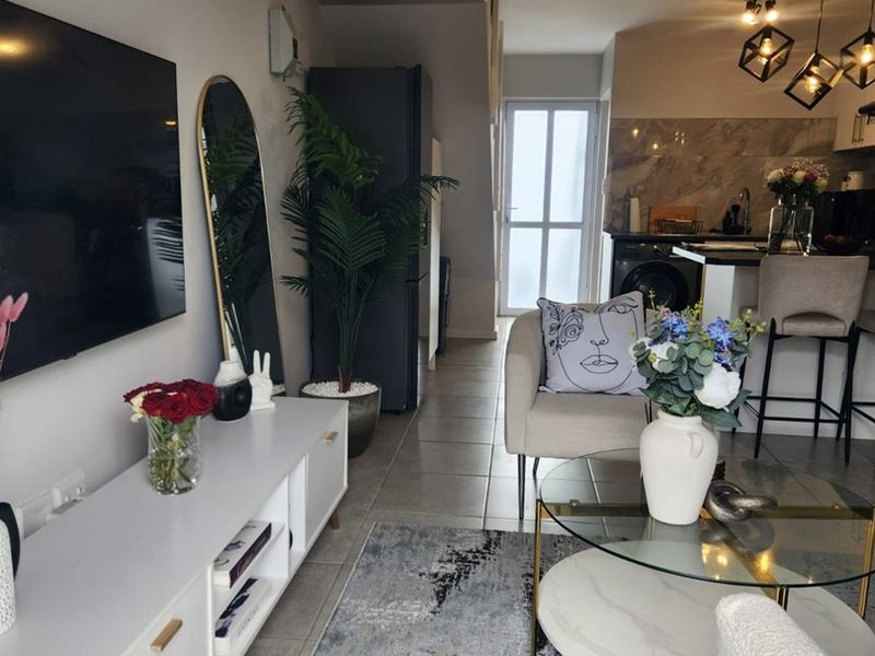 An open-plan living and kitchen area featuring tiled flooring, modern pendant lighting, and a sleek kitchen with stone backsplash and integrated cabinetry.