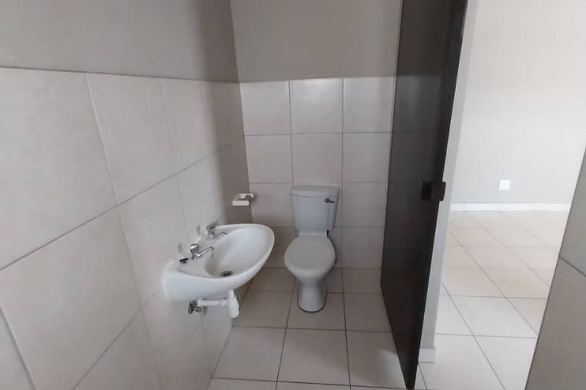 A compact bathroom featuring neutral wall tiles, a wall-mounted basin, and a standard toilet, accessible via a sliding door.