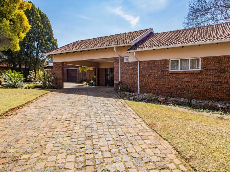 Front view of a brick house featuring a covered carport and a cobblestone driveway set within a landscaped garden.