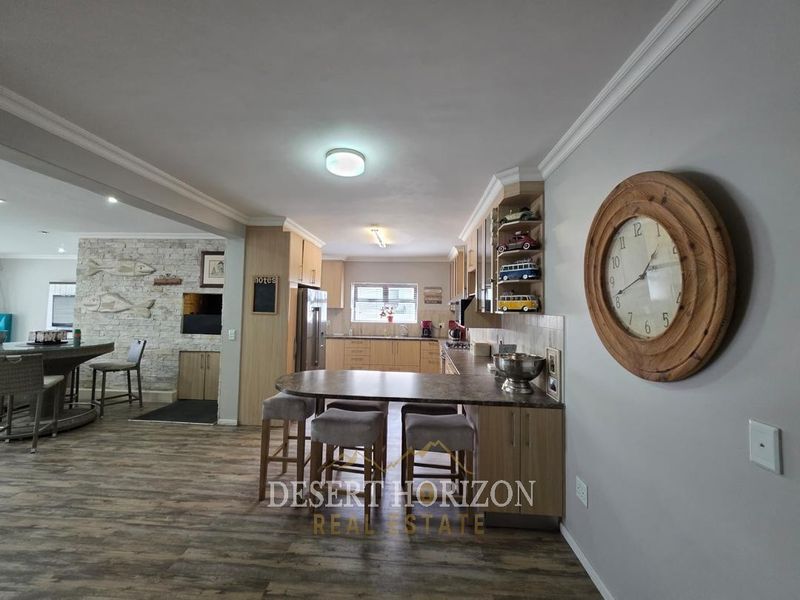 Open-plan kitchen and living area featuring modern laminate flooring, extensive built-in cabinetry, a breakfast bar, and a decorative stone veneer feature wall.