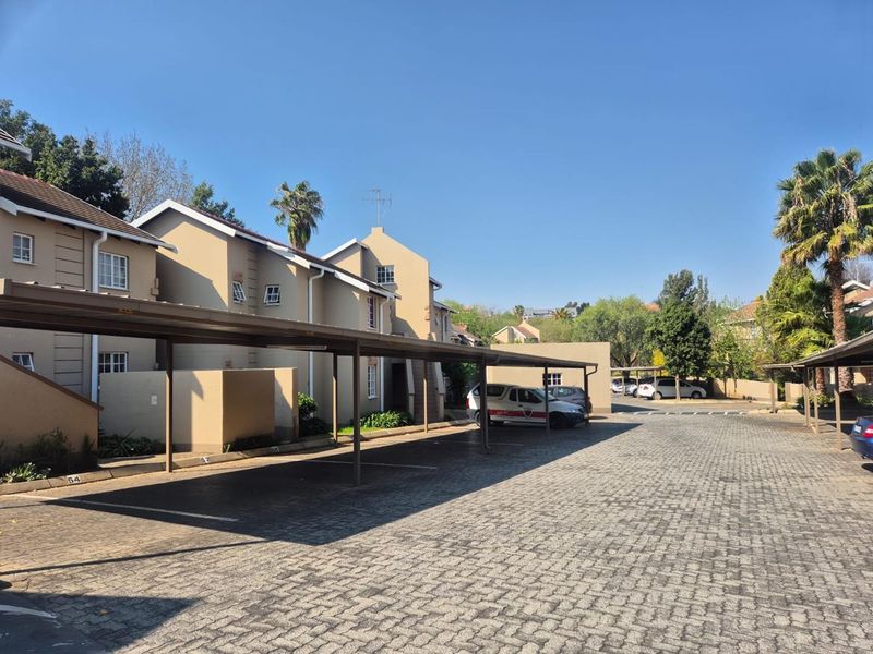 Exterior view of an apartment complex featuring covered parking bays and a paved driveway area.