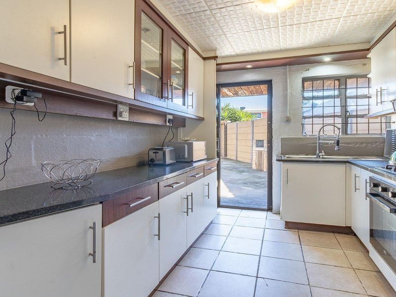 A functional kitchen featuring built-in cabinetry, granite countertops, a gas hob, and an integrated oven, with direct access to the rear exterior area.