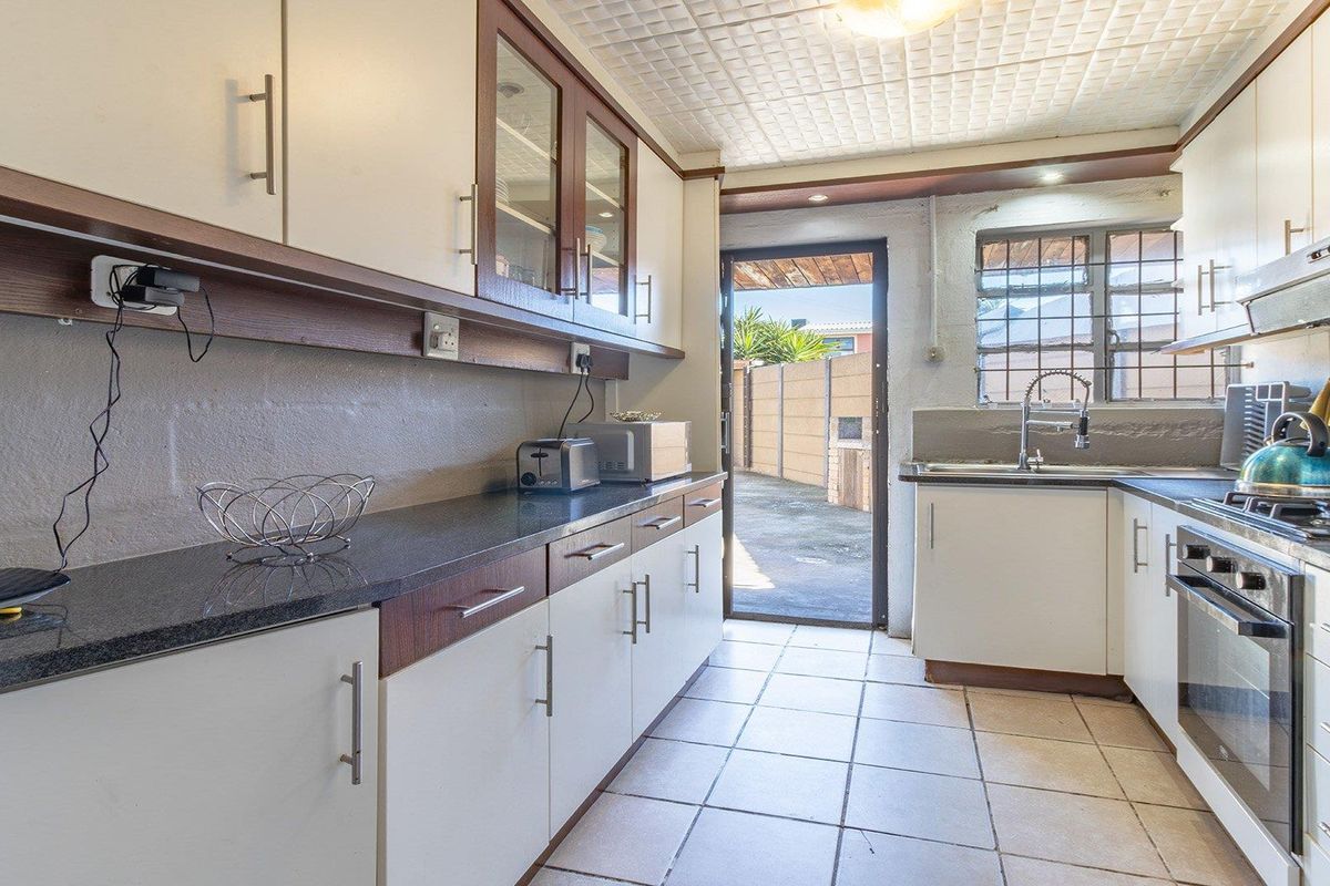 A functional kitchen featuring built-in cabinetry, granite countertops, a gas hob, and an integrated oven, with direct access to the rear exterior area.