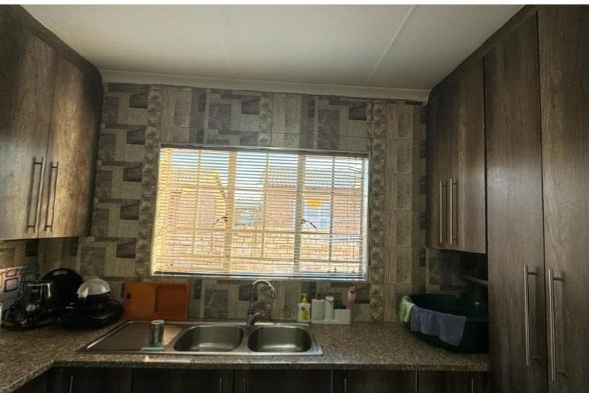 A functional kitchen featuring dark wood-look cabinetry, a double bowl stainless steel sink, and patterned tiled backsplash with natural light from the window.