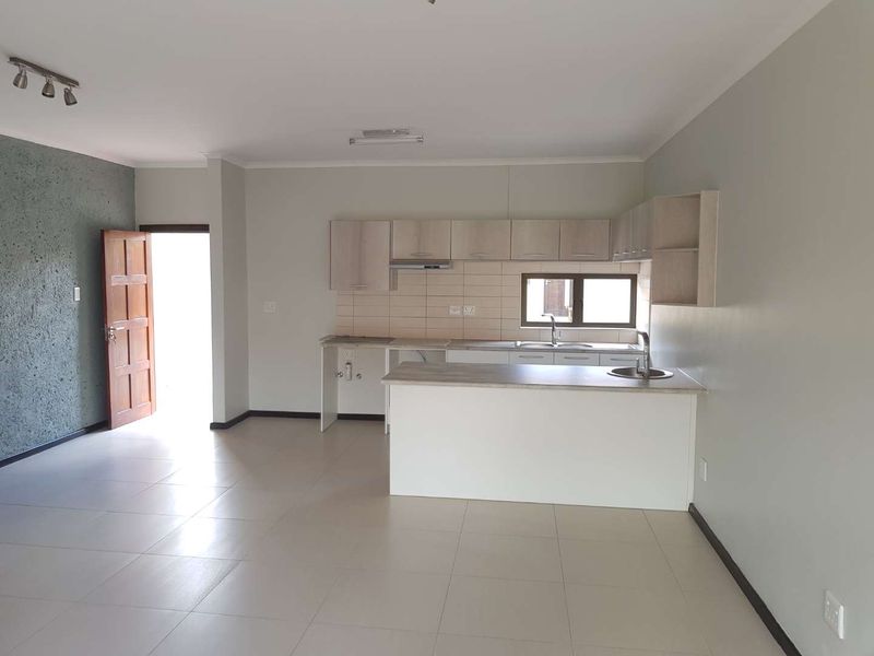 An open-plan living and kitchen area featuring neutral tiled flooring, built-in cabinetry, a breakfast bar, and direct access to the exterior.