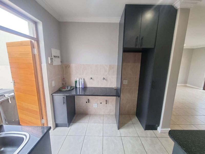 A functional laundry area featuring granite countertops, built-in dark cabinetry, tiled splashbacks, and dedicated plumbing connections for appliances.