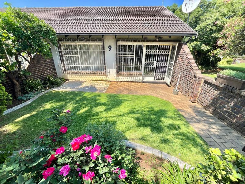 Front view of a townhouse featuring a paved patio, small lawn, and secure entrance with metal security gates.