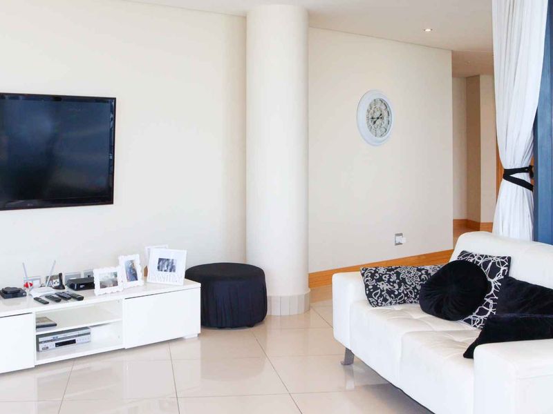 A bright living room featuring large windows with ocean views, tiled flooring, and a structural column, creating an open and airy atmosphere.