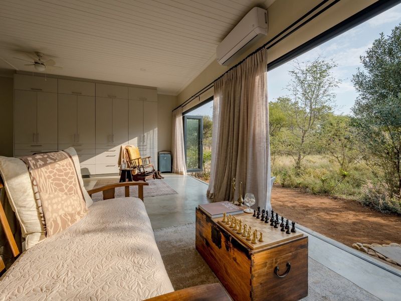 A bright living room featuring polished concrete floors, extensive built-in cabinetry, and large sliding glass doors that open to a natural outdoor landscape.