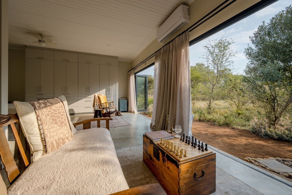 A bright living room featuring polished concrete floors, extensive built-in cabinetry, and large sliding glass doors that open to a natural outdoor landscape.
