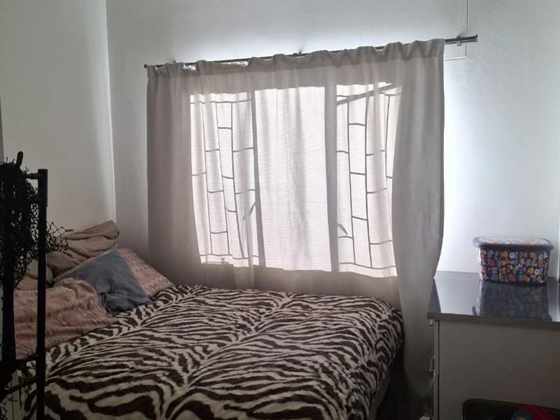 A functional bedroom featuring tiled flooring and a window with a curtain rod, providing a simple and practical living space.
