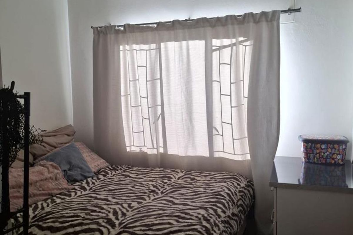 A functional bedroom featuring tiled flooring and a window with a curtain rod, providing a simple and practical living space.