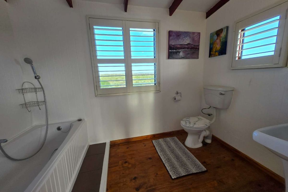 A bathroom featuring a bathtub with handheld shower, toilet, and basin, finished with timber flooring and white panelled walls.