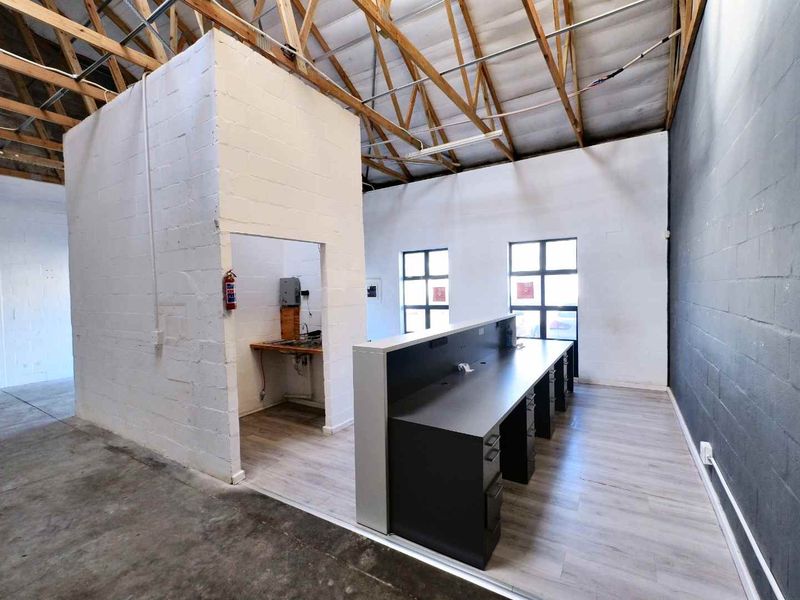Industrial office space featuring exposed timber roof trusses, concrete block walls, laminate flooring, and a built-in reception desk area.