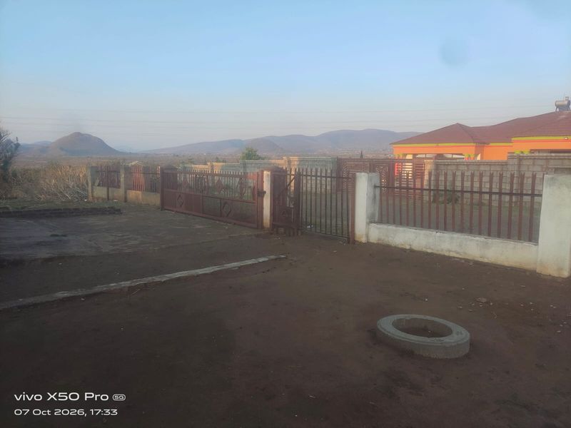 Front exterior view of the property featuring a metal gate, perimeter fencing, and a concrete driveway with mountain views in the background.