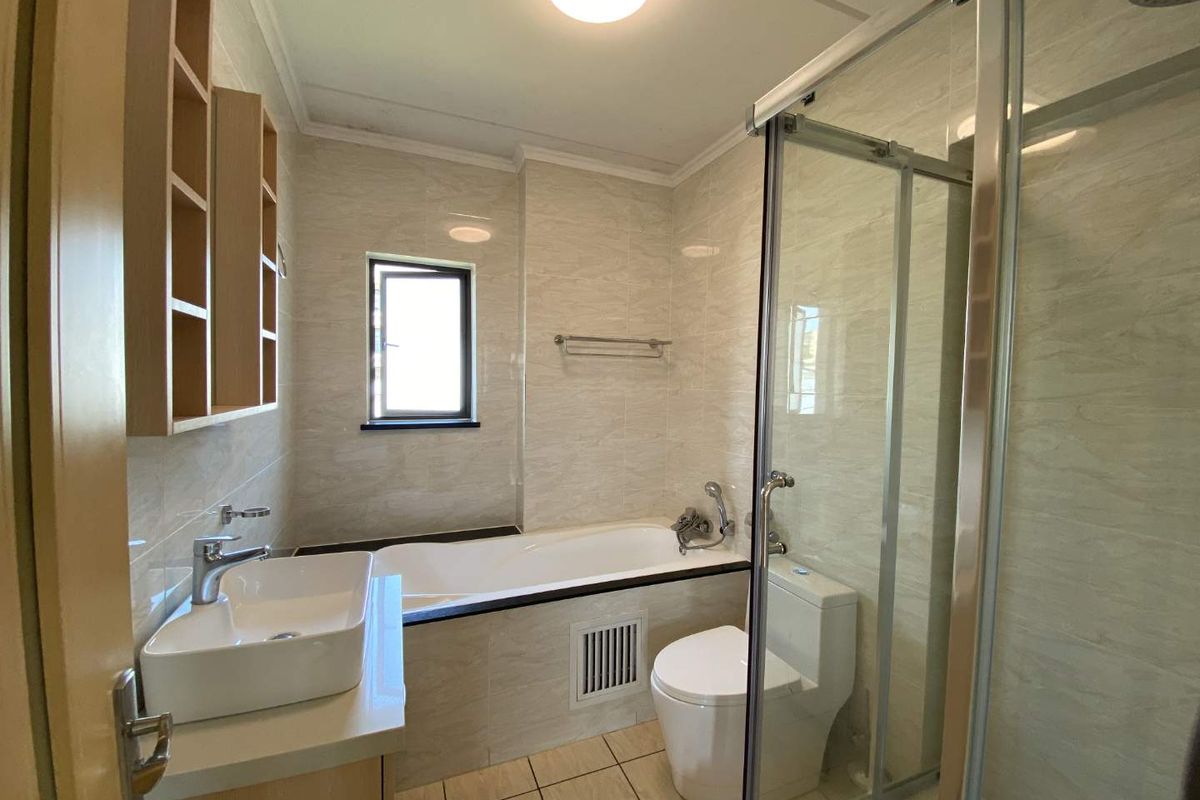 A modern bathroom featuring a glass-enclosed shower, a built-in bathtub, a vanity basin, and neutral wall tiling.