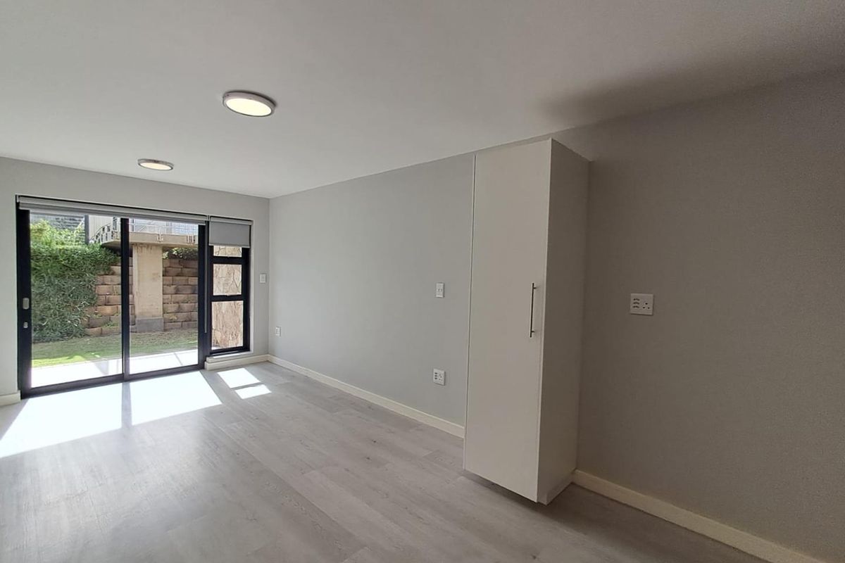 A bright, modern living area featuring light wood-look flooring, recessed ceiling lighting, and large sliding glass doors providing access to the outdoor space.