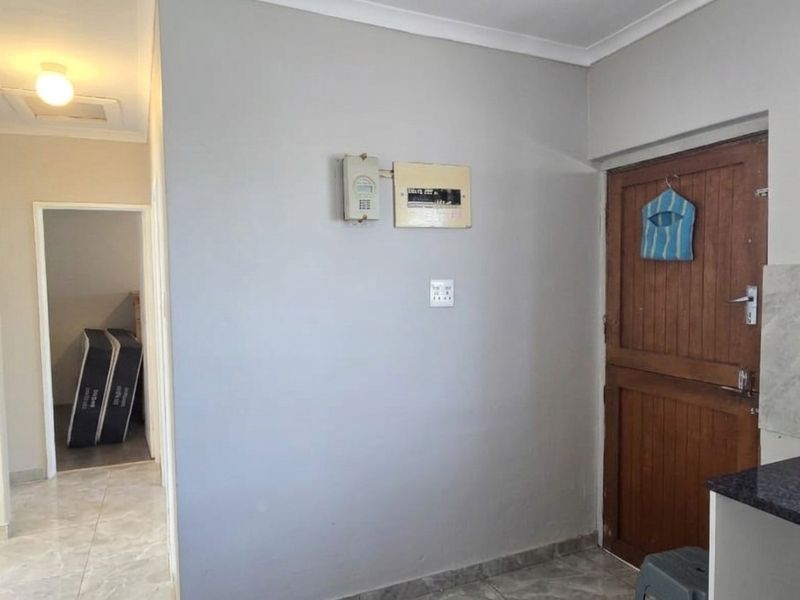 A functional kitchen area featuring tiled flooring, a stone countertop, and a timber door, with an integrated electrical distribution board and prepaid meter.