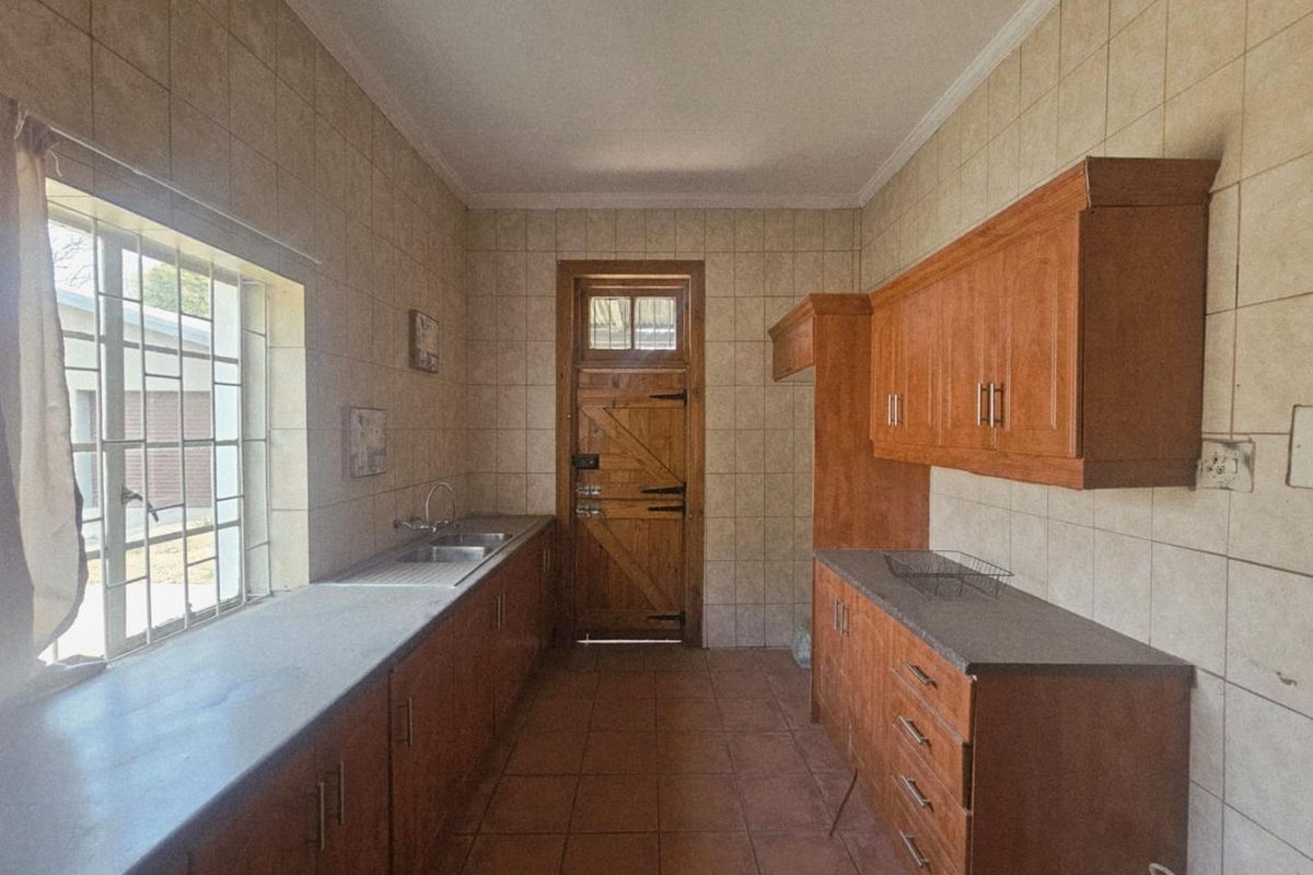 A functional kitchen featuring wooden cabinetry, tiled walls, and a stainless steel sink, providing a practical workspace with direct exterior access.