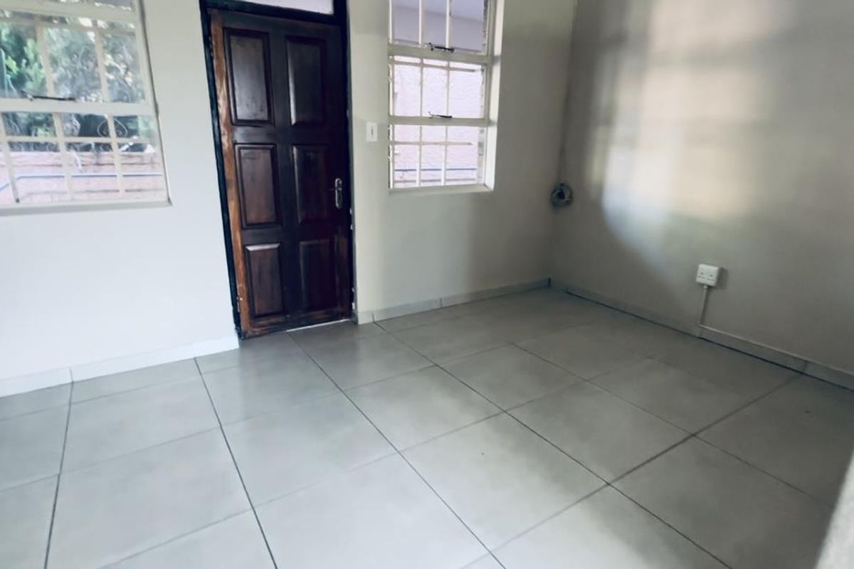 An empty living area featuring neutral tiled flooring, large windows for natural light, and a solid timber entrance door.