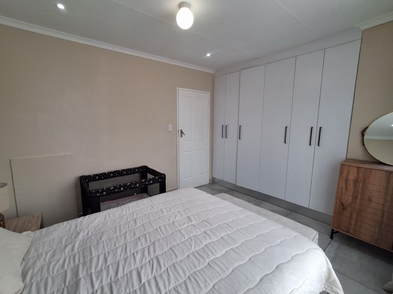 A well-maintained bedroom featuring neutral wall tones, tiled flooring, and extensive white built-in cupboards providing ample storage space.