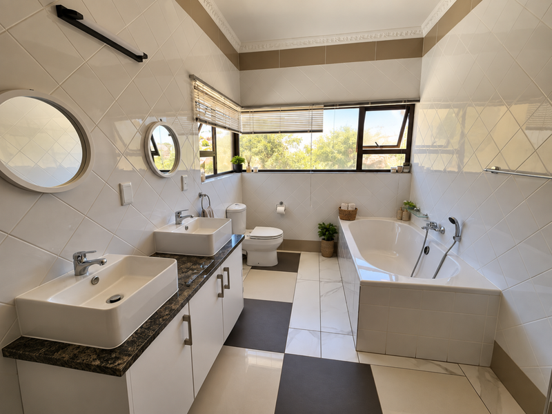 A bright, modern bathroom featuring a double vanity with vessel sinks, a built-in bathtub, and large-format tiled flooring with a contrasting pattern.