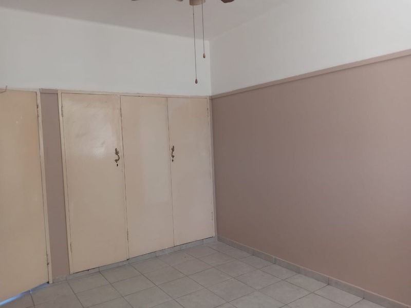 An empty bedroom featuring tiled flooring, a ceiling fan, and built-in cupboards with a two-tone wall finish.