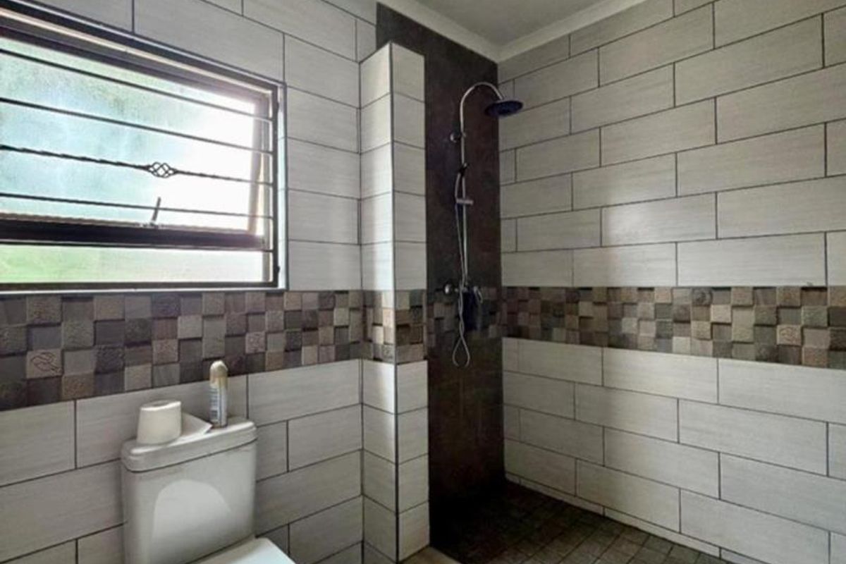 A modern bathroom featuring a walk-in shower with dark accent tiling, a white toilet, and neutral wall tiles with a decorative mosaic border.