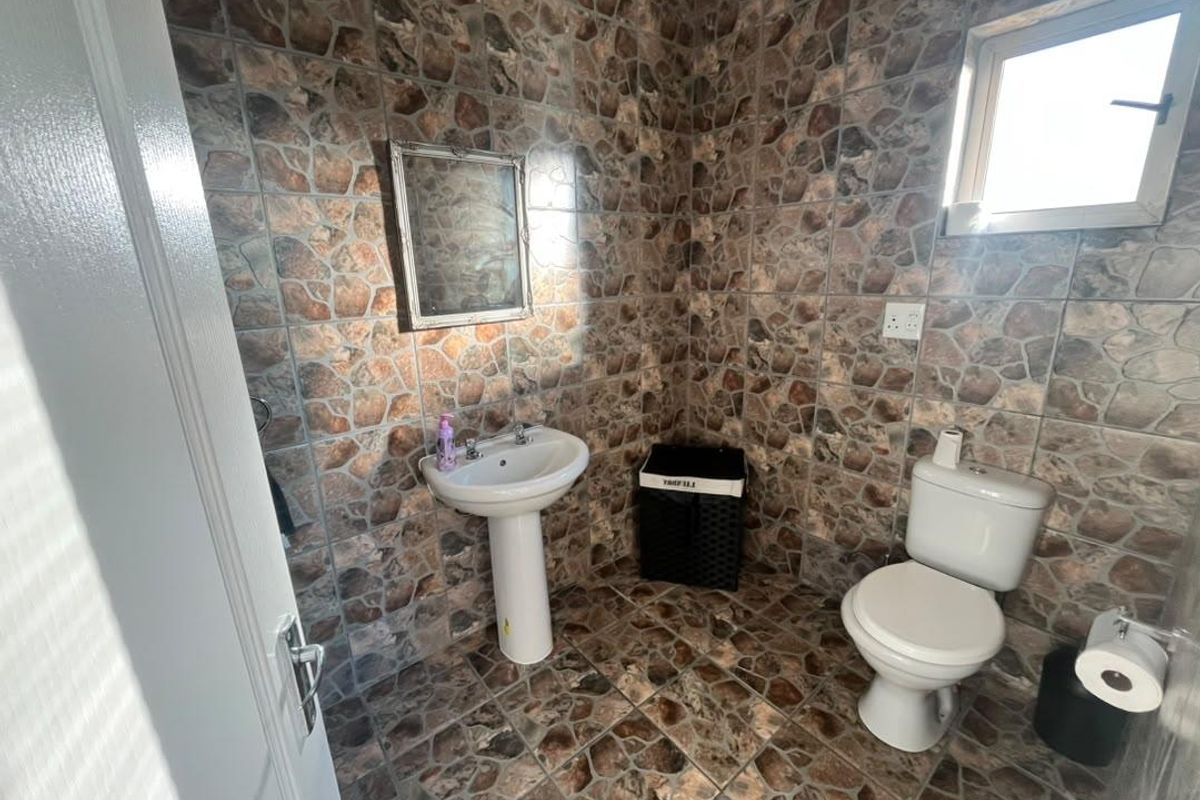 A compact bathroom featuring full-height stone-effect wall and floor tiling, a white pedestal basin, and a standard toilet.