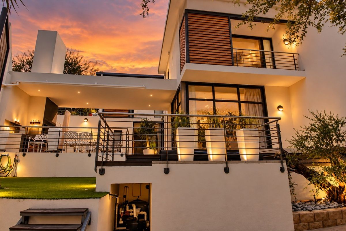 Modern townhouse rear elevation featuring a spacious covered patio, elevated balcony with metal railings, and integrated architectural lighting at dusk.