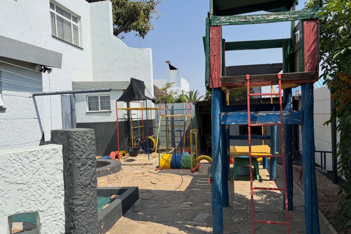 Rear courtyard area featuring stone paving and plastered exterior walls, currently utilized as a play area with various fixed outdoor structures.