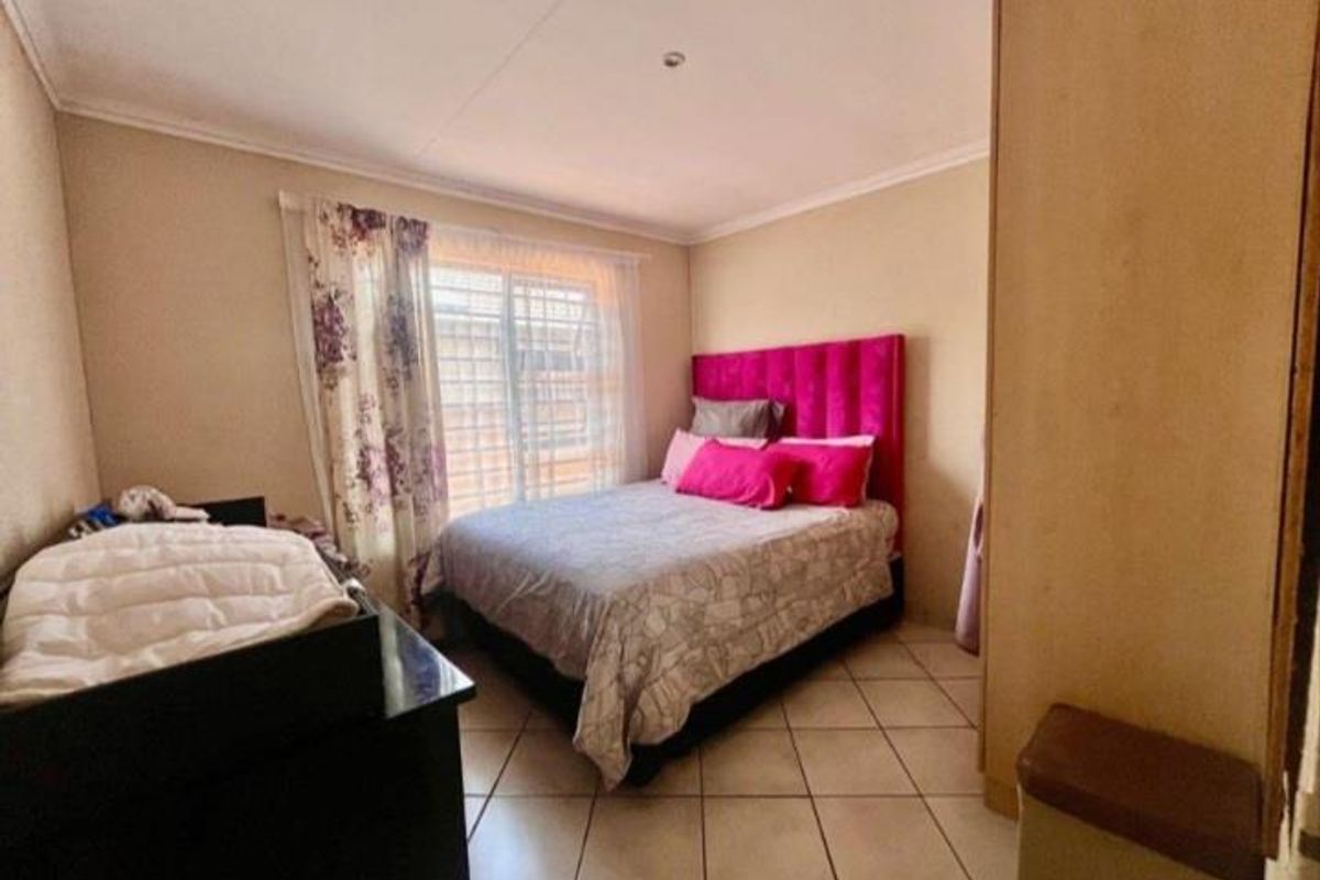 A functional bedroom featuring tiled flooring, a window with security bars, and built-in storage space.