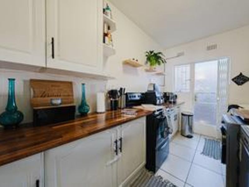 A functional kitchen featuring white cabinetry, warm wooden countertops, and tiled flooring, with direct access to an outdoor area through a security gate.