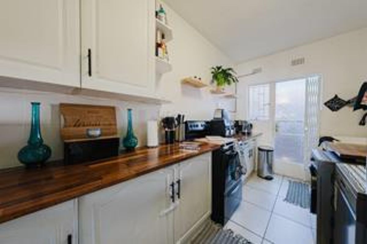 A functional kitchen featuring white cabinetry, warm wooden countertops, and tiled flooring, with direct access to an outdoor area through a security gate.