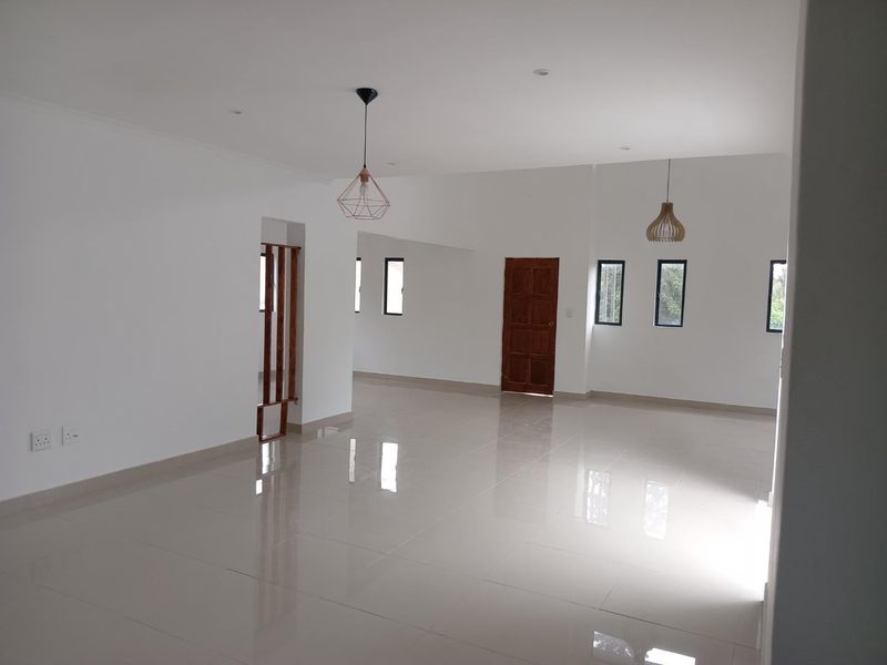 A spacious, bright, and empty living area featuring polished tiled flooring, modern pendant lighting, and a timber room divider.
