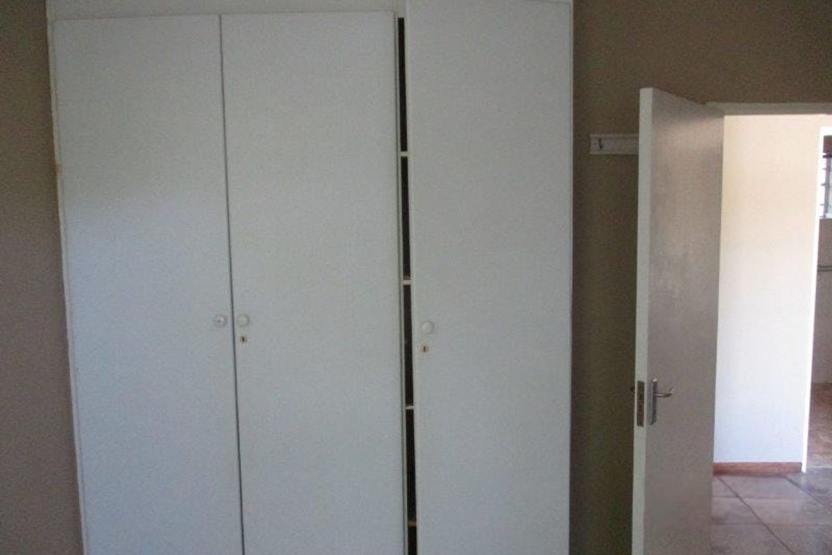 A bedroom interior featuring built-in white wardrobes and a standard internal door leading to an adjacent tiled space.
