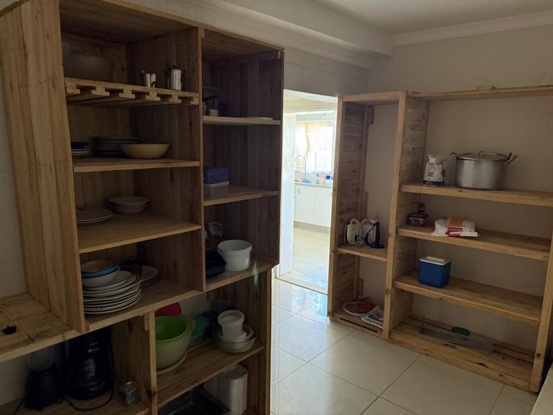 A functional scullery area featuring tiled flooring and extensive built-in wooden shelving for storage, with a view through to the kitchen.