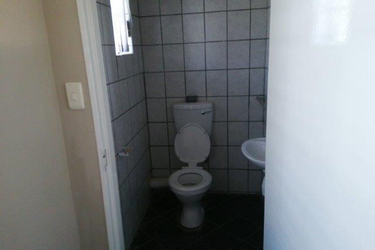 A compact office restroom featuring tiled walls, a standard toilet, and a wall-mounted basin.