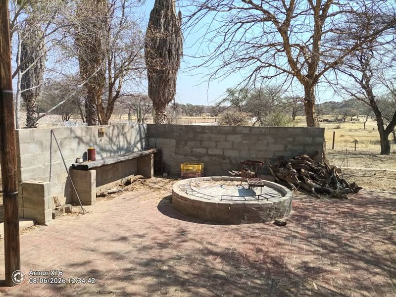 Outdoor entertainment area featuring a circular stone fire pit, built-in concrete bench, and brick paving, set within a natural small holding landscape.