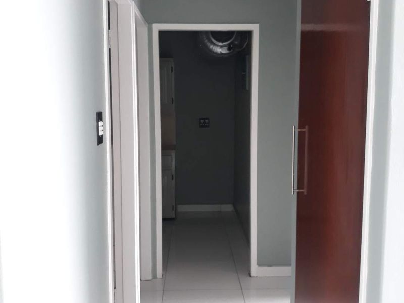 A clean, neutral-toned hallway featuring tiled flooring and access to adjacent rooms, providing a functional transition space within the apartment.