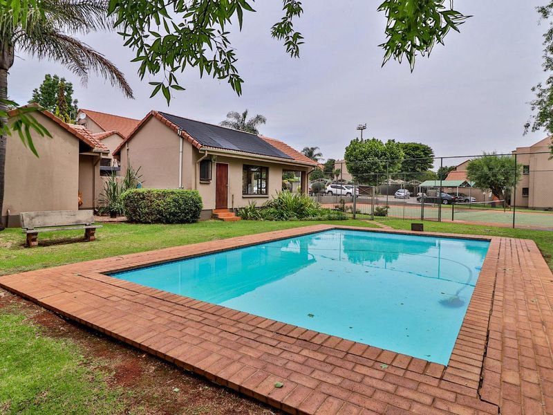Outdoor pool area featuring a swimming pool with brick coping, adjacent to a communal tennis court and landscaped garden space.