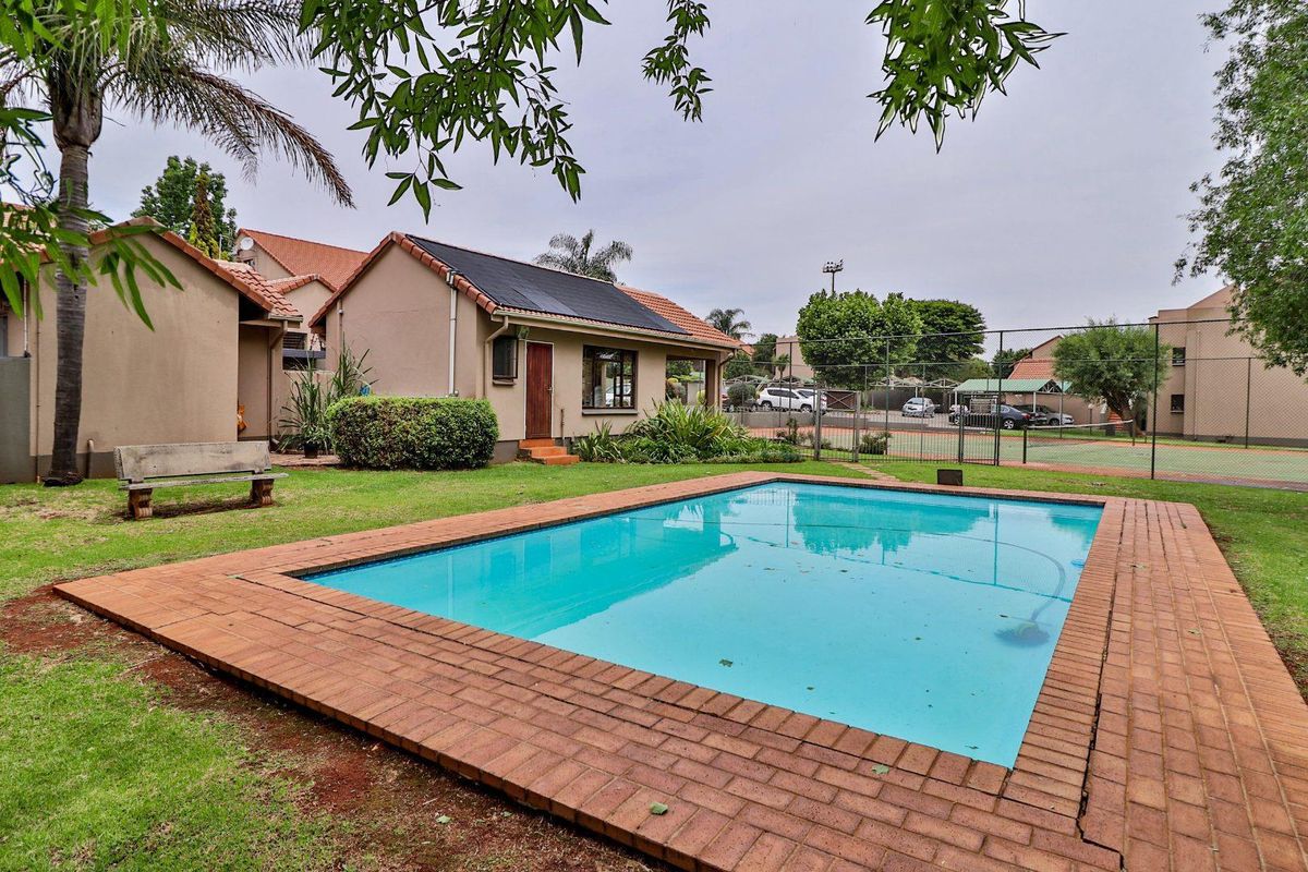 Outdoor pool area featuring a swimming pool with brick coping, adjacent to a communal tennis court and landscaped garden space.