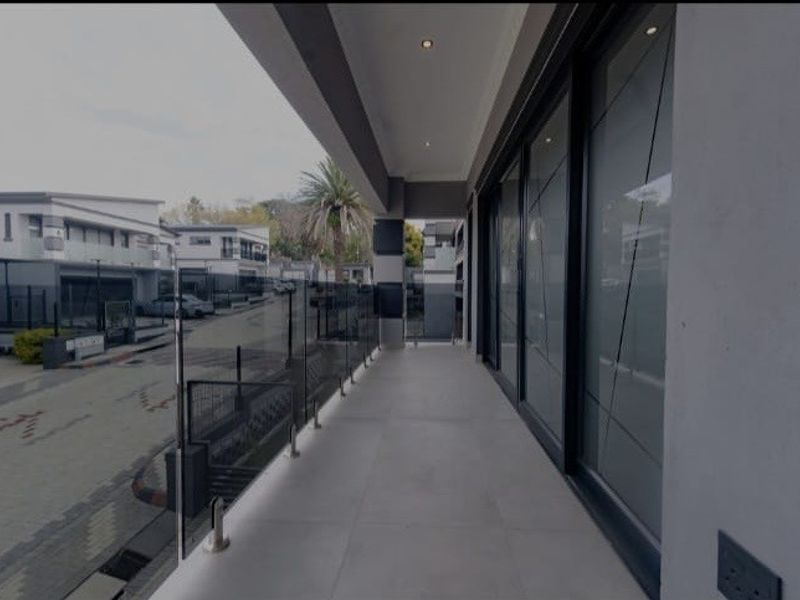 A modern, covered balcony featuring sleek glass balustrades, tiled flooring, and large sliding glass doors, offering a clean and contemporary outdoor living space.