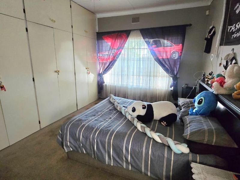 A bedroom featuring built-in cupboards, a ceiling fan, and carpeted flooring, offering a functional space with potential for modernization.