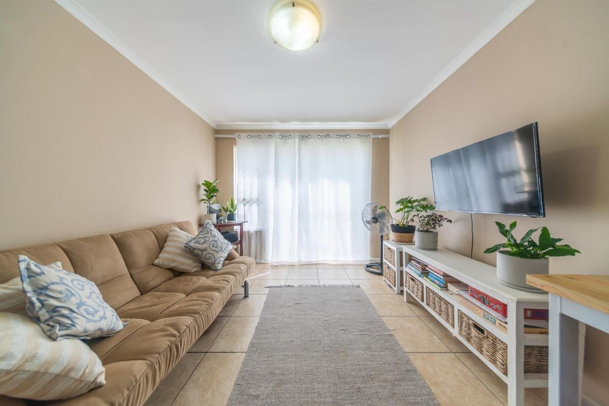 A comfortable living room featuring neutral wall tones, tiled flooring, and a large window with curtains, providing a bright and functional space.