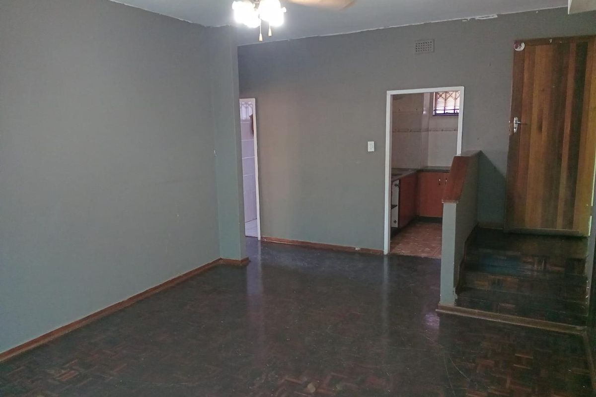 An empty living area featuring dark parquet flooring, a ceiling fan, and an internal staircase leading to a timber door.